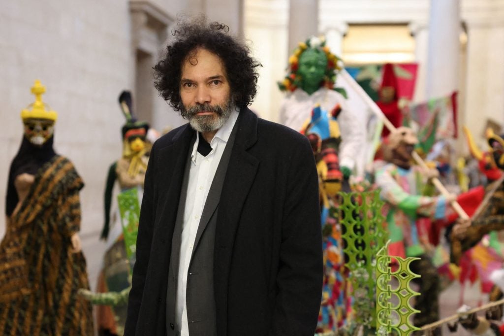 A black man stands in front of colorful sculptures