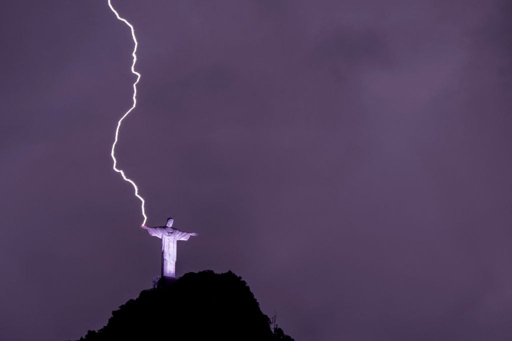 a dramatic photograph of lightning striking part of a statue atop a hill in Brazil