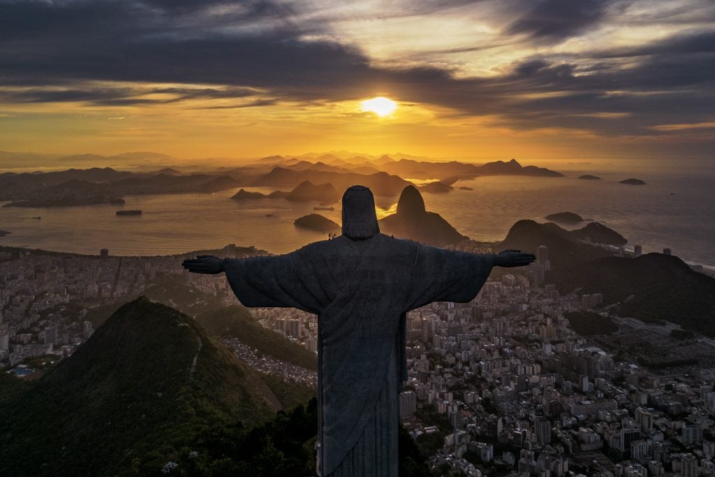 a photograph of the sun rising over Rio de Janeiro with the silhouette of christ in the foreground