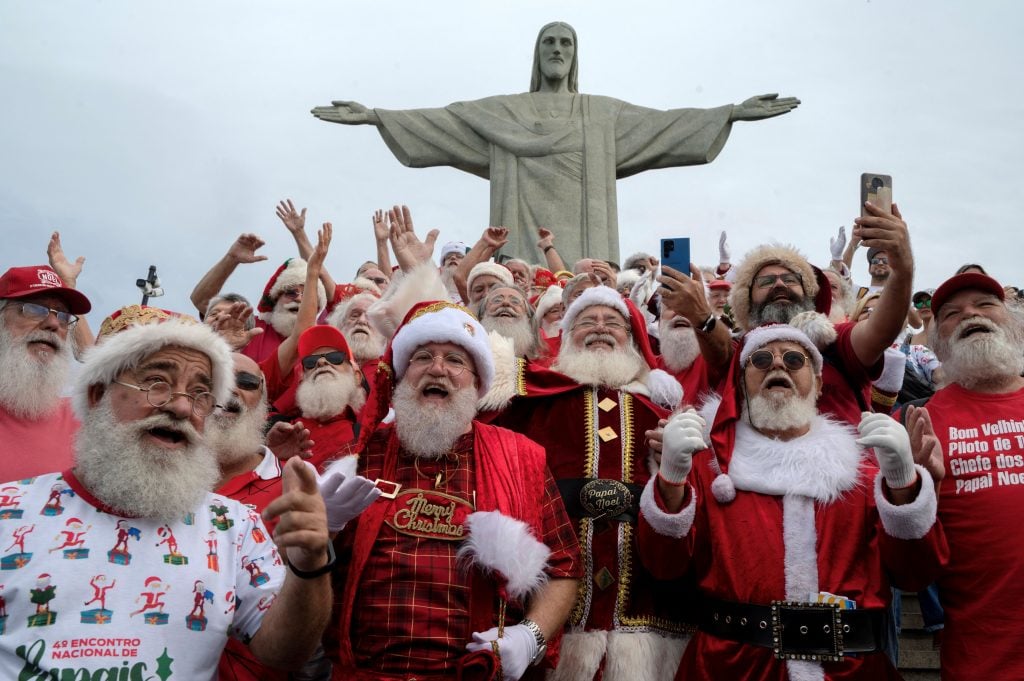 a group of men dressed like santa claus stand in front of a statue of christ