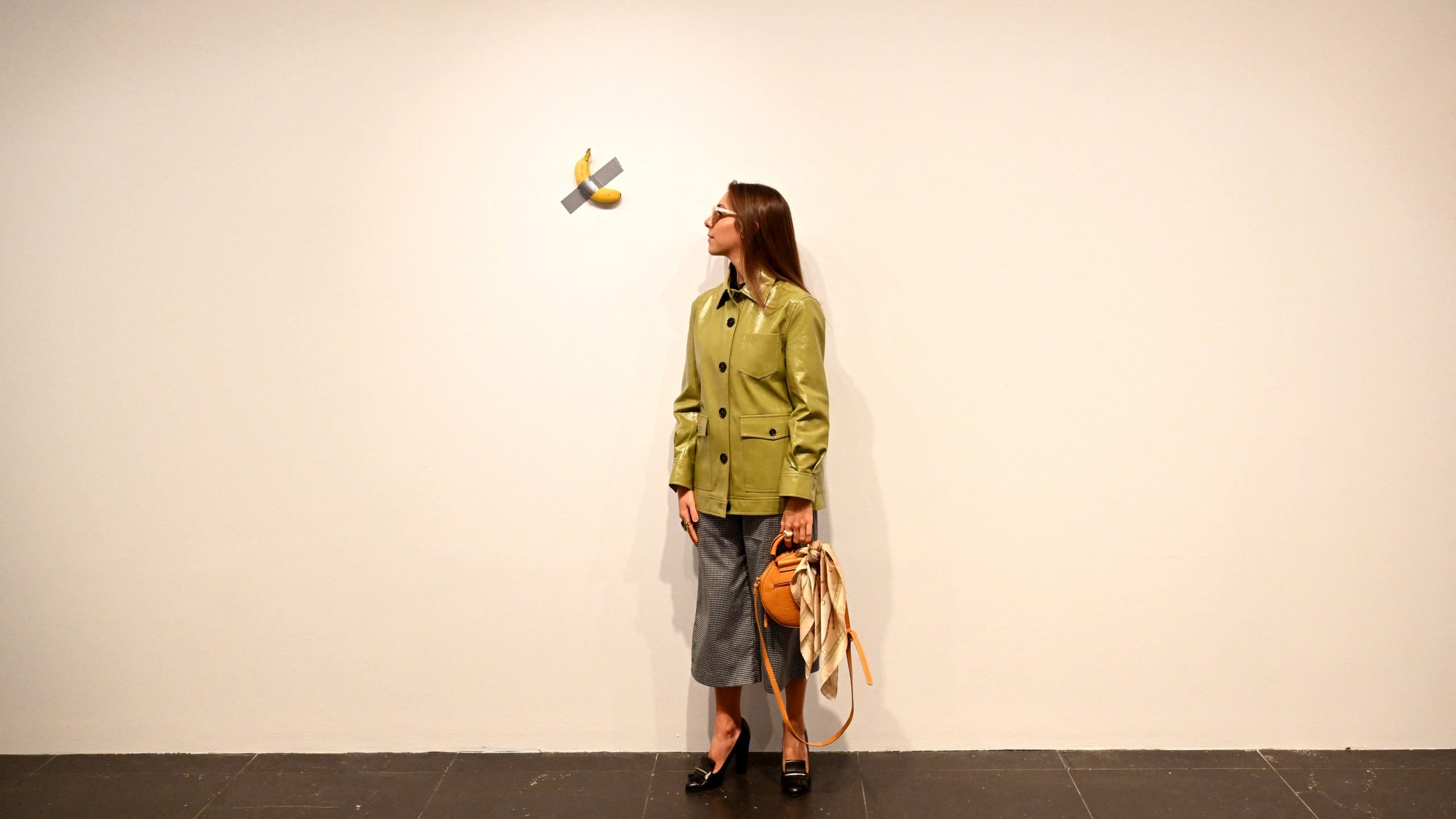 A woman stands next to a banana taped to a wall