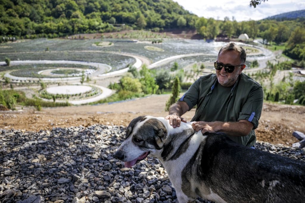 a man with a dog sits in front of a landscape of swirls