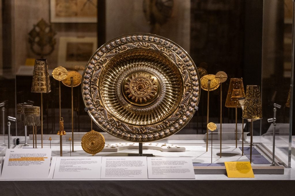 a gold disc with detailed engraving stands in a vitrine