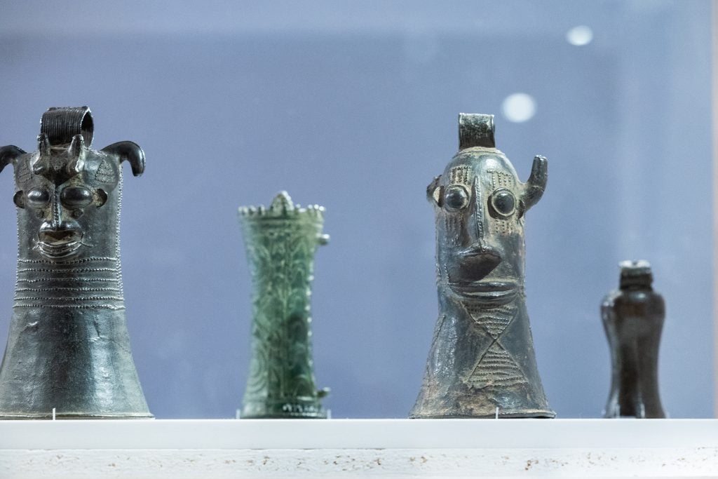 A display of ancient metallic and ceramic sculptures with stylized human faces and abstract designs in a museum setting