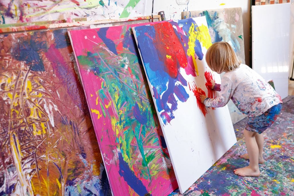 a small child dwarfed by tall canvases in a paint-splattered studio