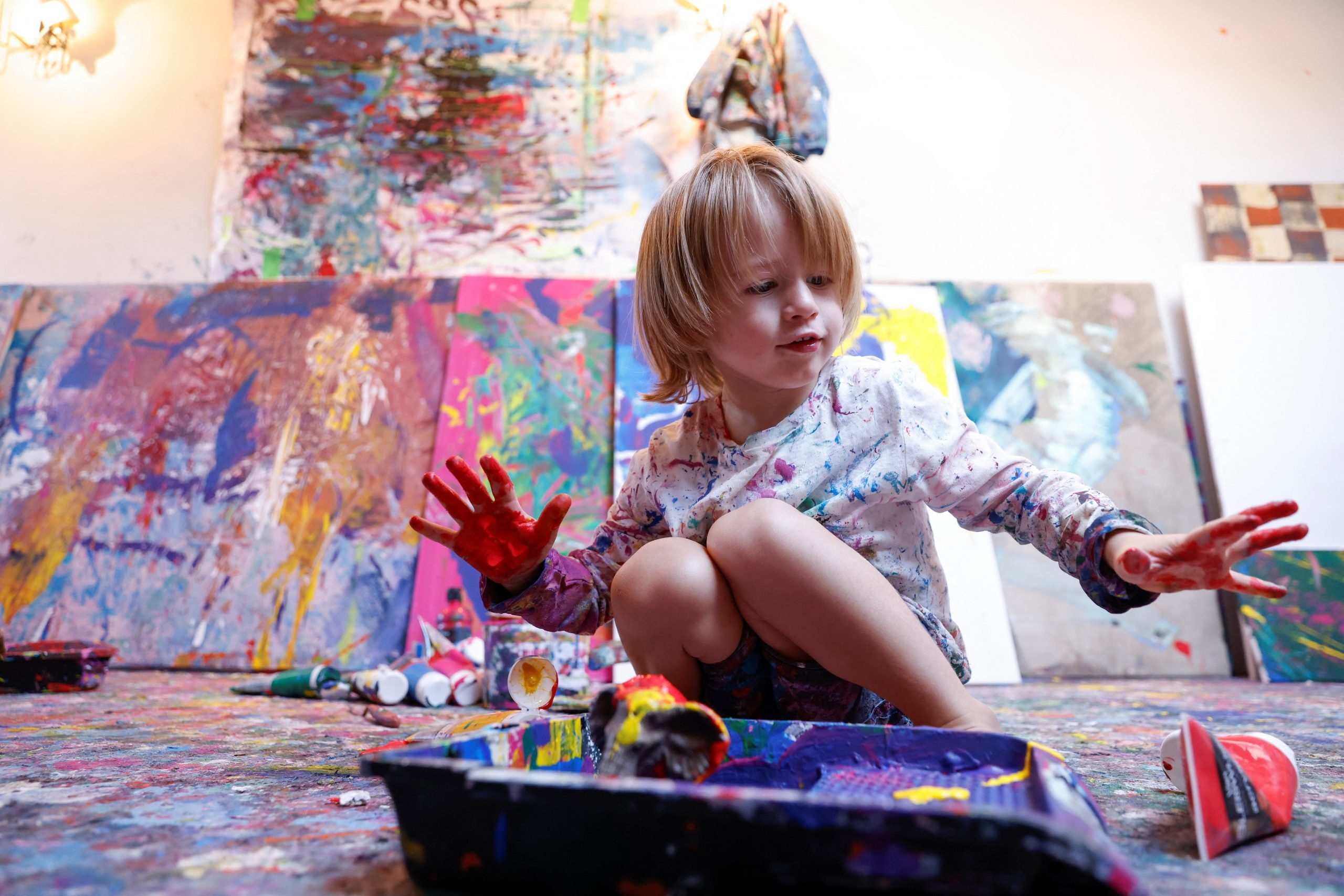 a small blonde child appears in a paint covered studio