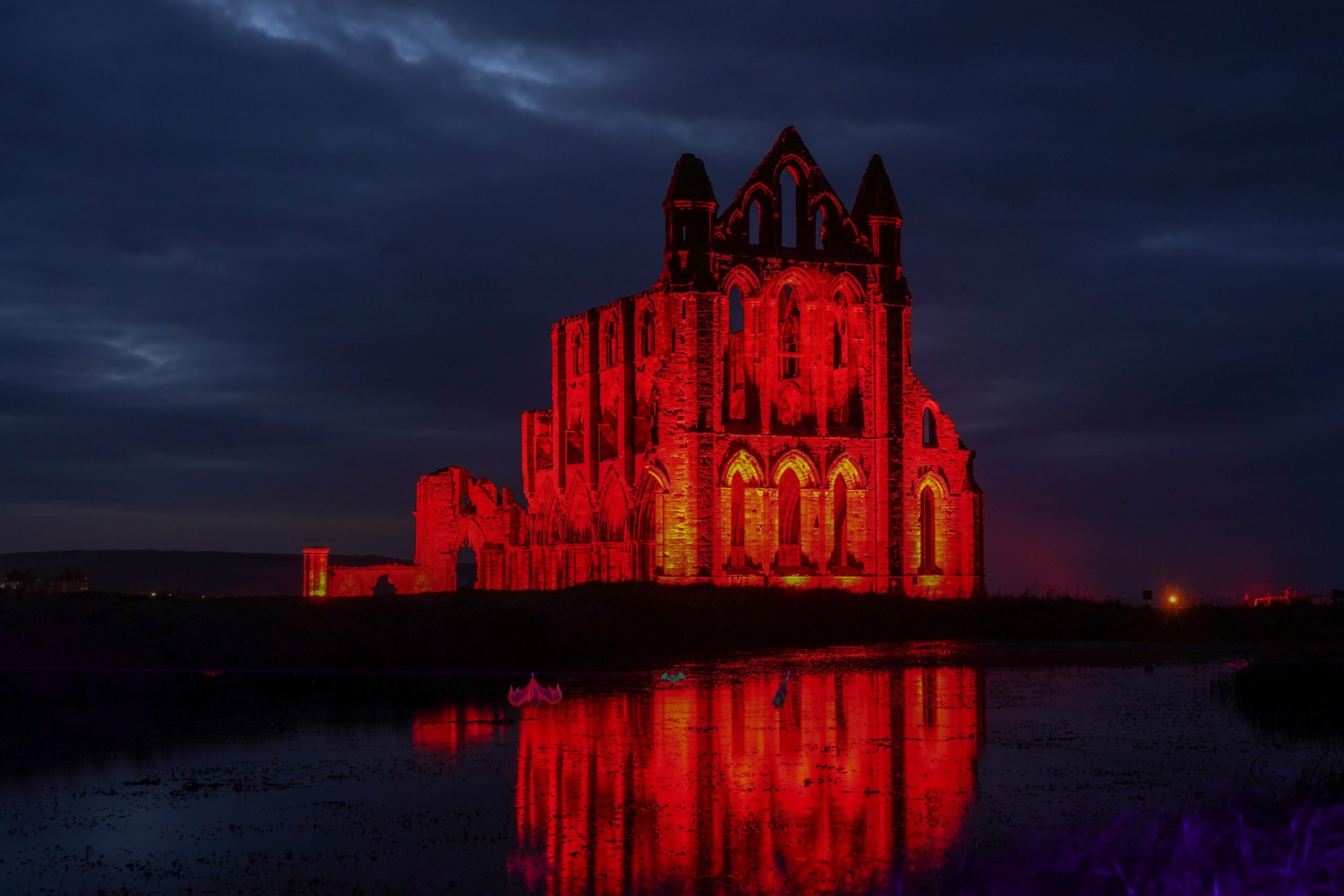 A castle overlooking a lake is lit up in red lights at nighttime