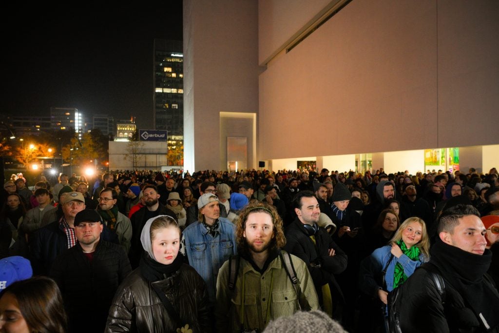 a large crowd of people stand outside of a large white building at night