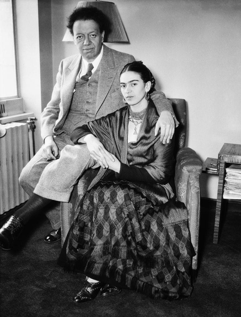 a black and white photo of a man and a woman seated on a chair.