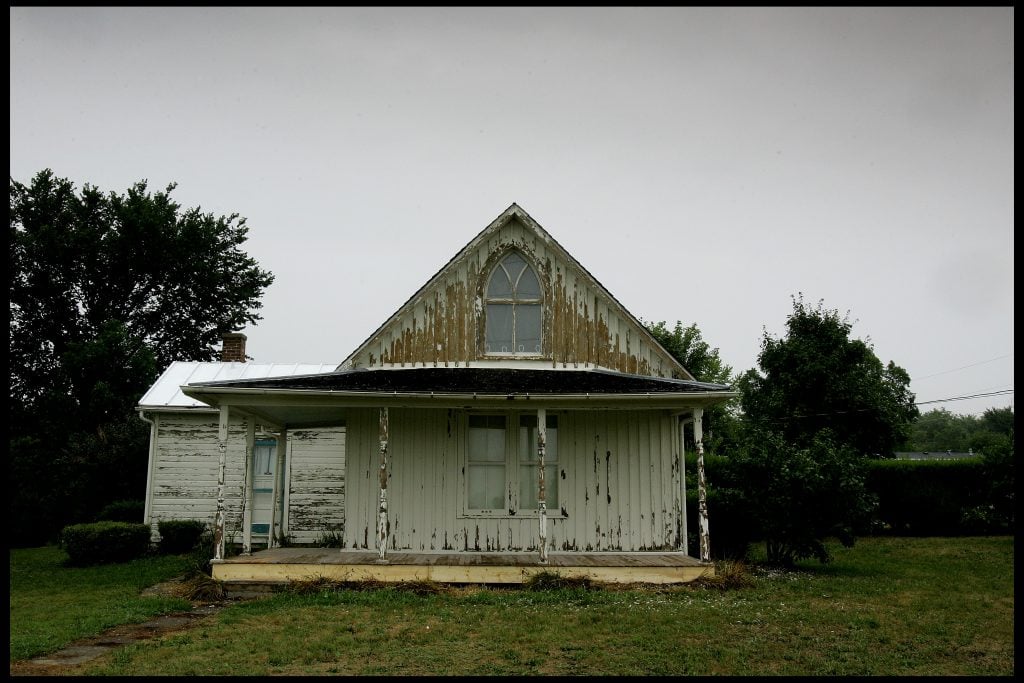 a ramshackle looking white house with a porch