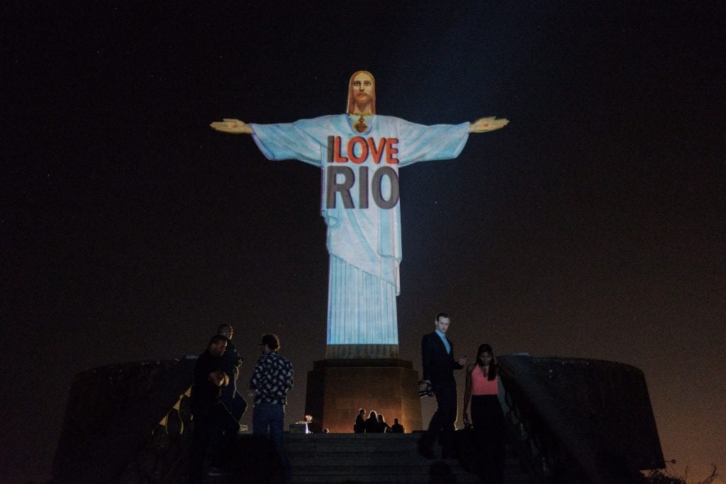 a statue of christ with outsretched arms has a projected shirt that reads 'i love rio'