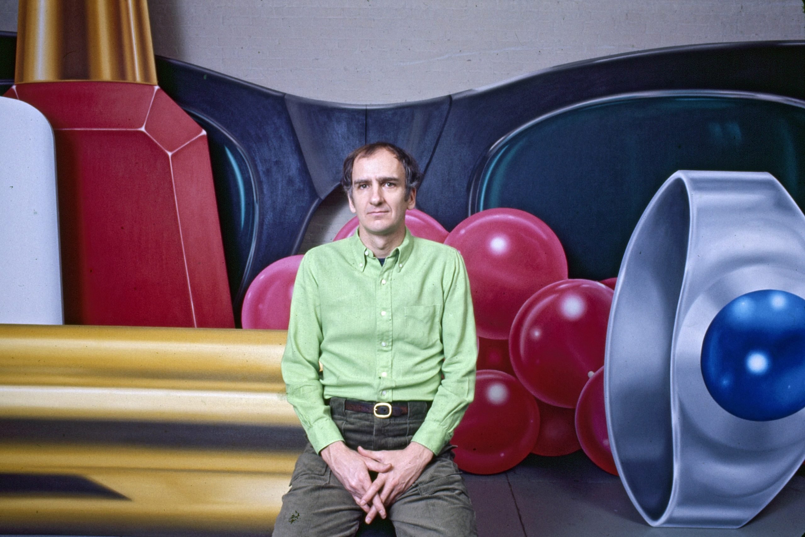 Artist Tom Wesselmann wears a green shirt and poses in front of his oversized imagery