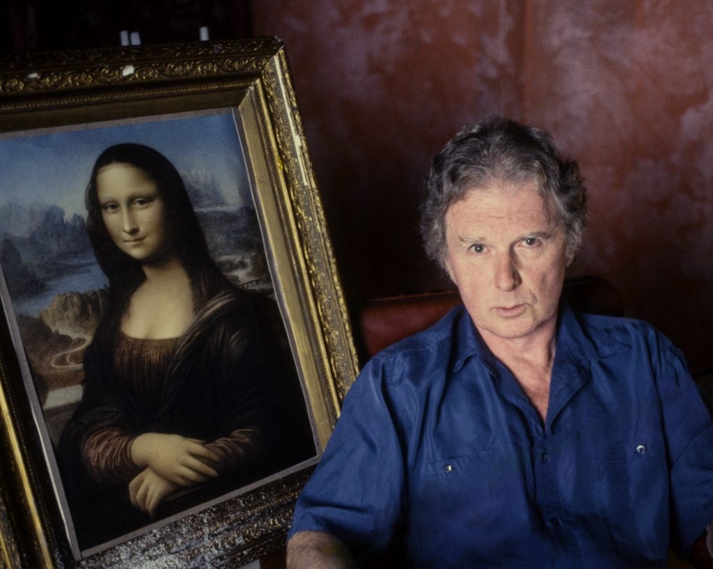 a color photograph of a white man sitting next to a copy of the mona lisa