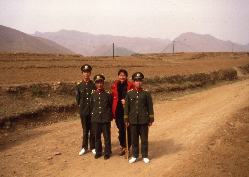 three uniformed men and a woman in a red coat stand on a path in the Chinese countryside