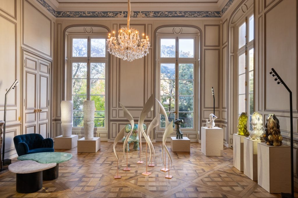 an ornate European sitting room is filled with design furniture and trees are visible in the windows 