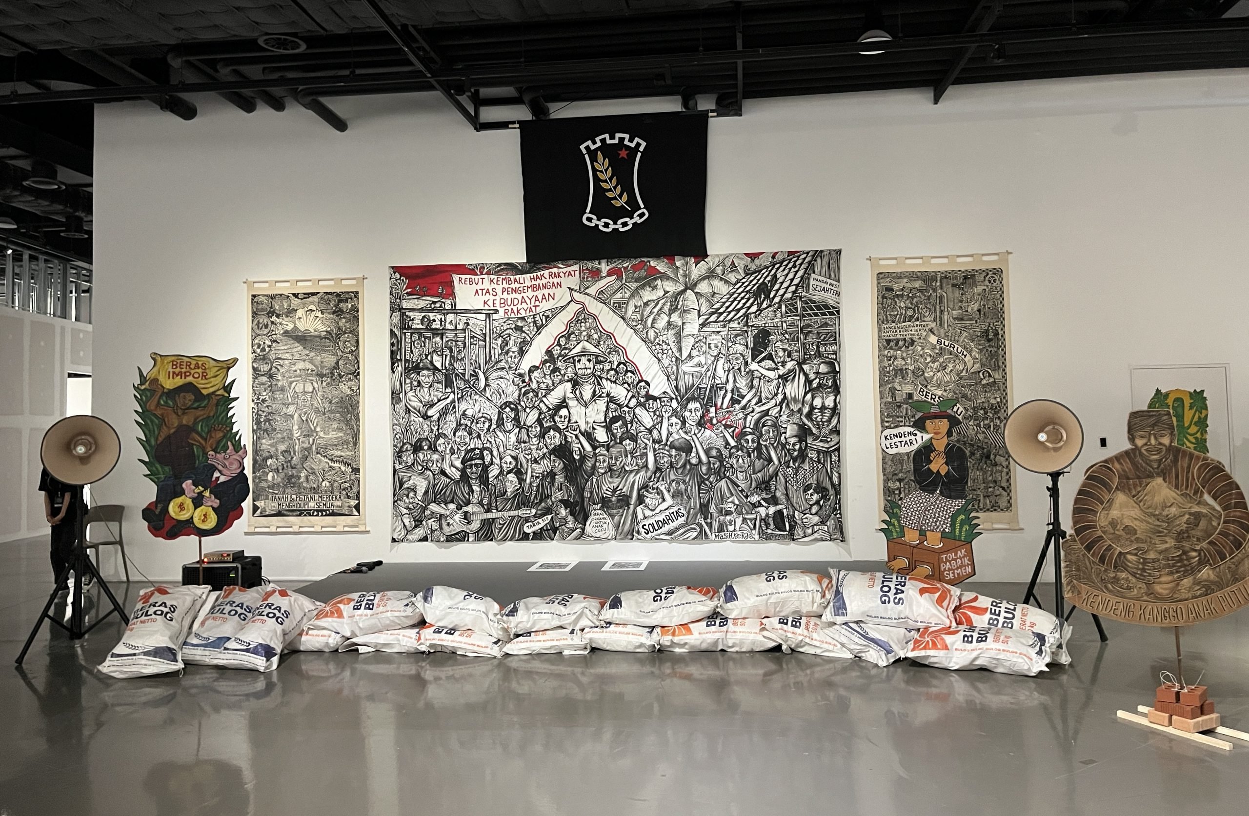 Black-and-white wall paintings cover a white wall, showing a large group of people protesting.