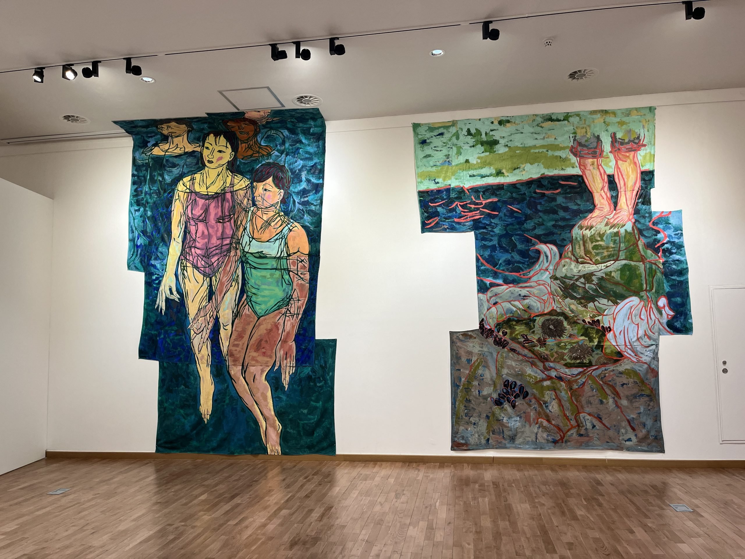 Two large paintings appear on a white wall. One shows two people in the water. The other shows feet standing in water.