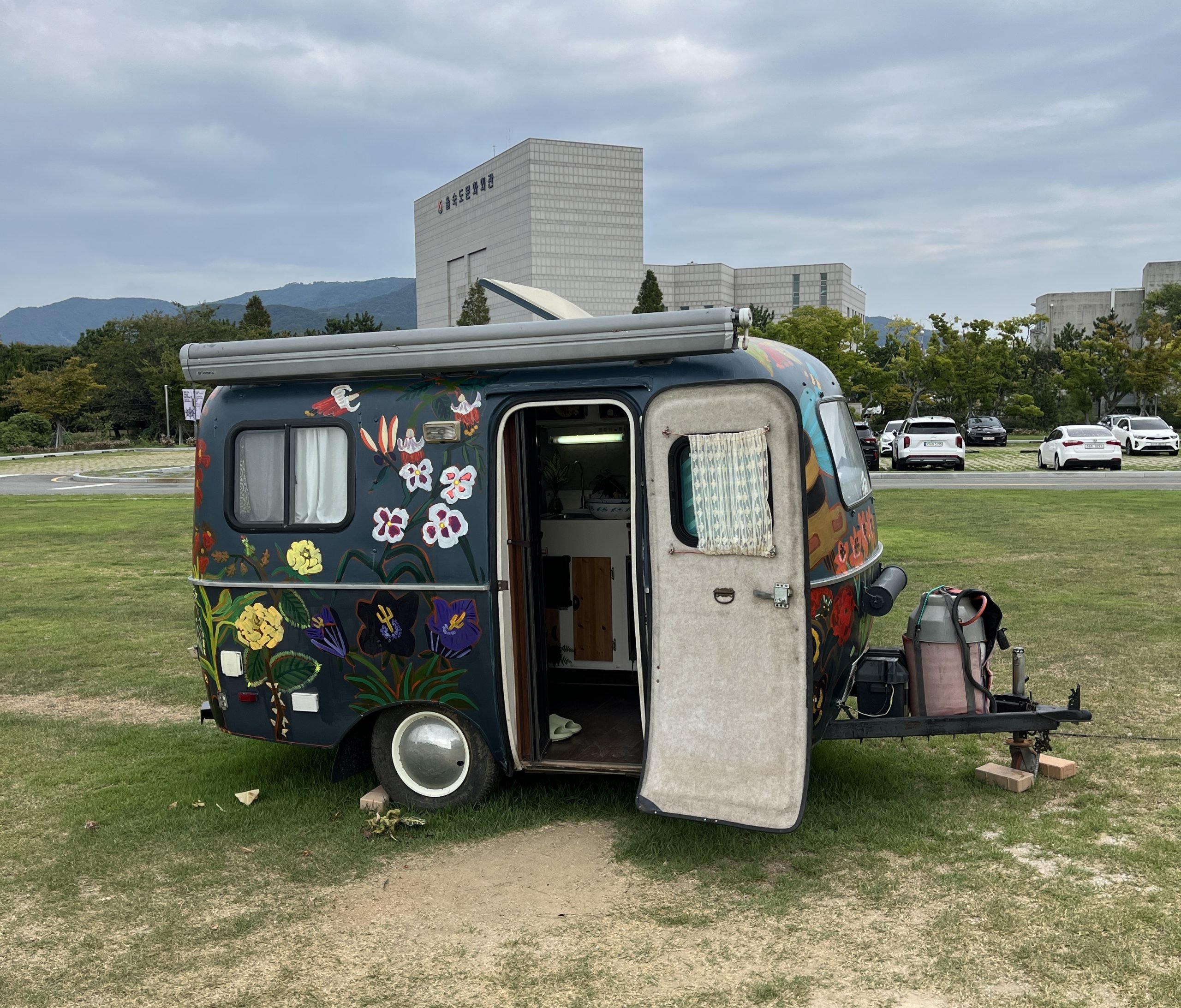 A tiny trailer home sits in a park with one door open.