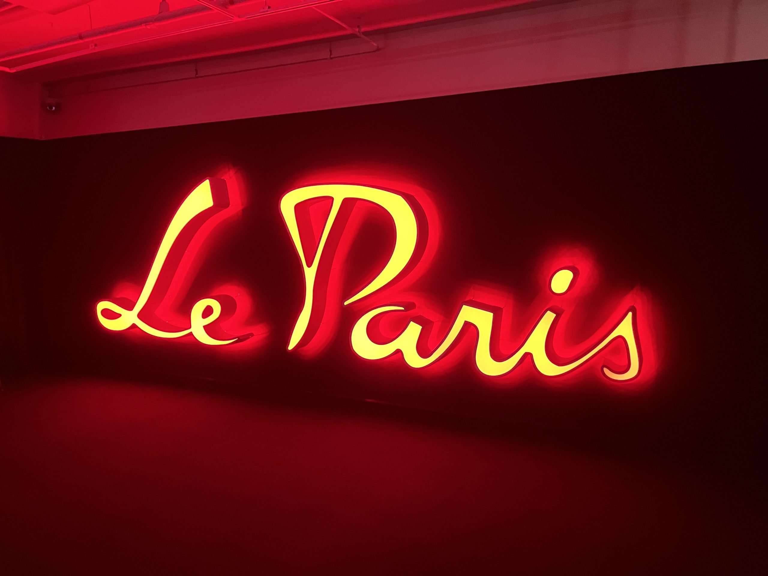 A large red electric sign reads, in cursive, "Le Paris."