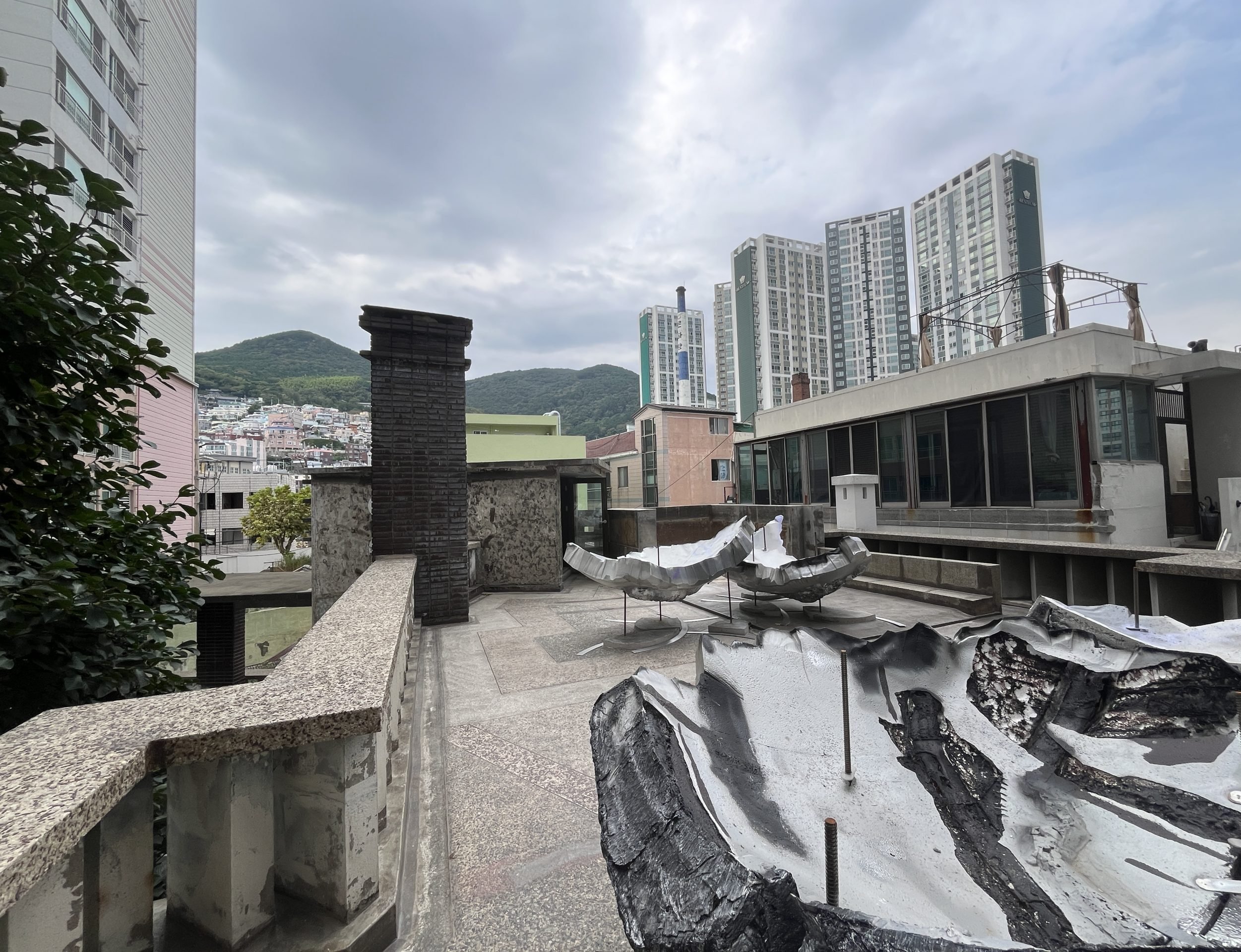 A skyline is seen from a rooftop holding craggily sculptures