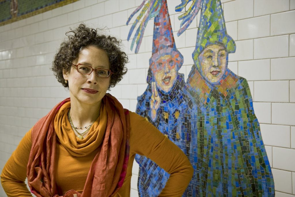 a woman stands in the subway station, the tiles behind her are a mosaic of two NYE revelers