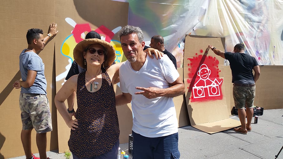 a woman and a man stand next to each other, arms slung over each other, posing for the photo. the man makes a peace sign