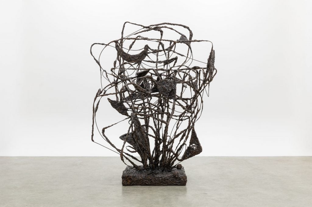 a sculpture by Rashid Johnson composed of twisting broze wires to form a skeletal mask sits in a gallery