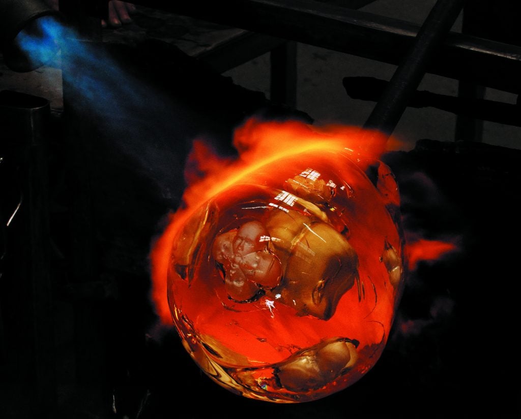 a molten glass orb with plastic faces embedded within it floats in a black space