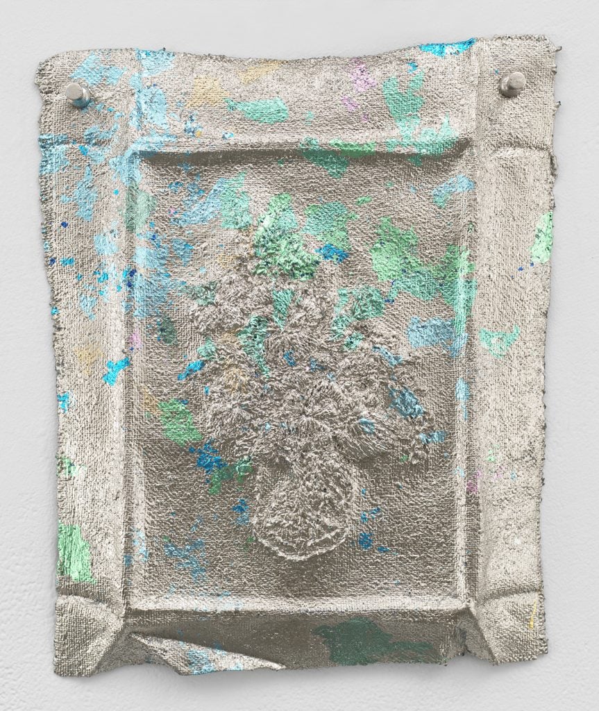 Jessie Henson, Monument (c.p.). A bronze cast sculpture of a rectangular embroidery cast in bronze with a silver metallic coating.