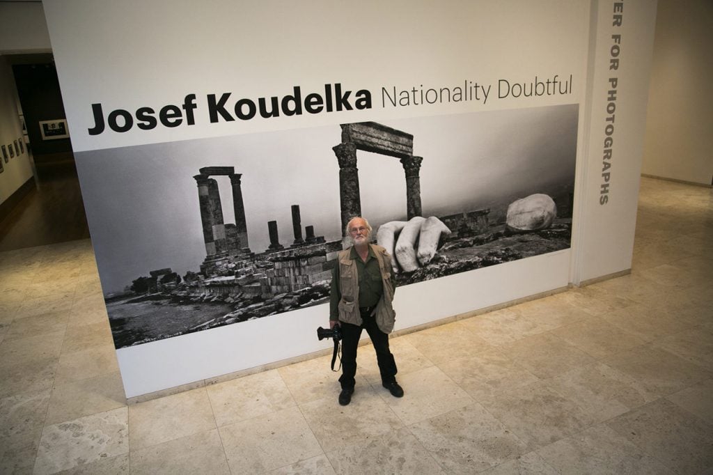 A man stands with a camera in front of a black and white photographic wallpaper