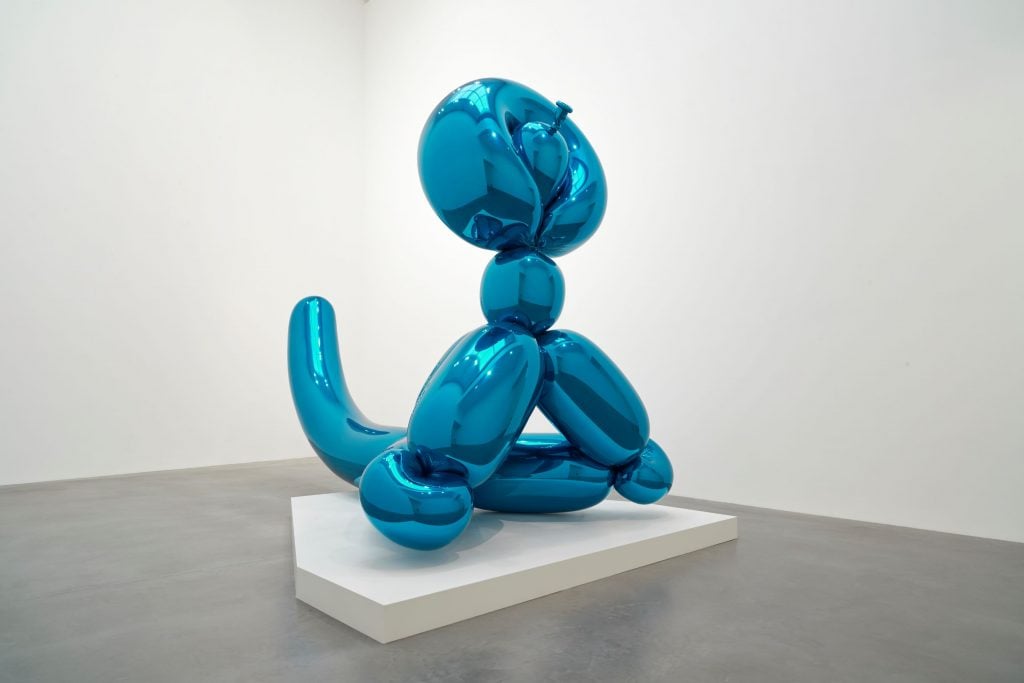 A shiny blue sculpture of a balloon monkey is seen in a white space