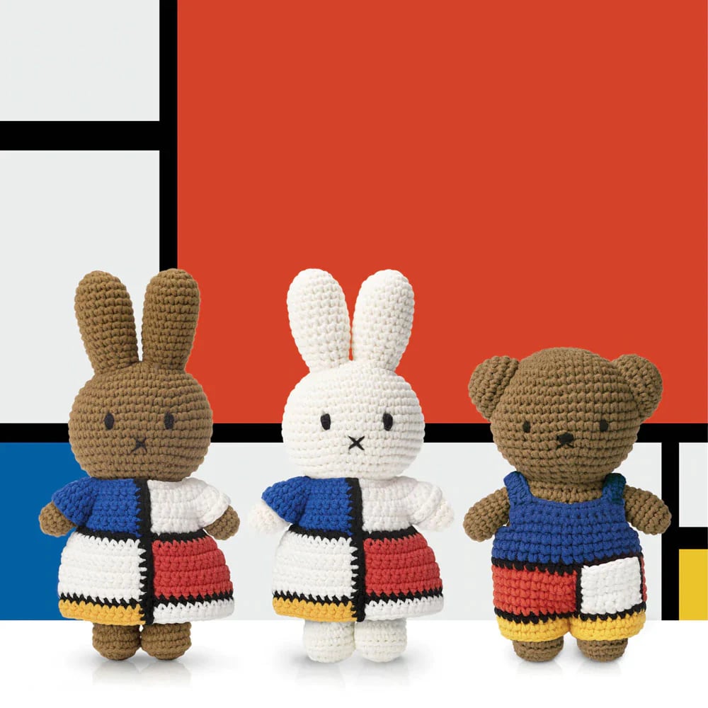 Three crochet stuffed animals dressed in outfits inspired by Piet Mondrian's abstract primary color grid paintings, standing in front of a Mondrian-inspired design. 