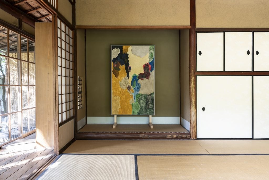 A serene Japanese-style room with tatami mats, shoji screens, and a vibrant abstract painting displayed on a green wall alcove.