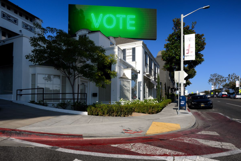 Nancy Baker Cahill, Body Politic (2024) on a billboard on the Sunset Strip in Hollywood. A billboard shows an image of a green neon sign reading "Vote" against a blue sky.