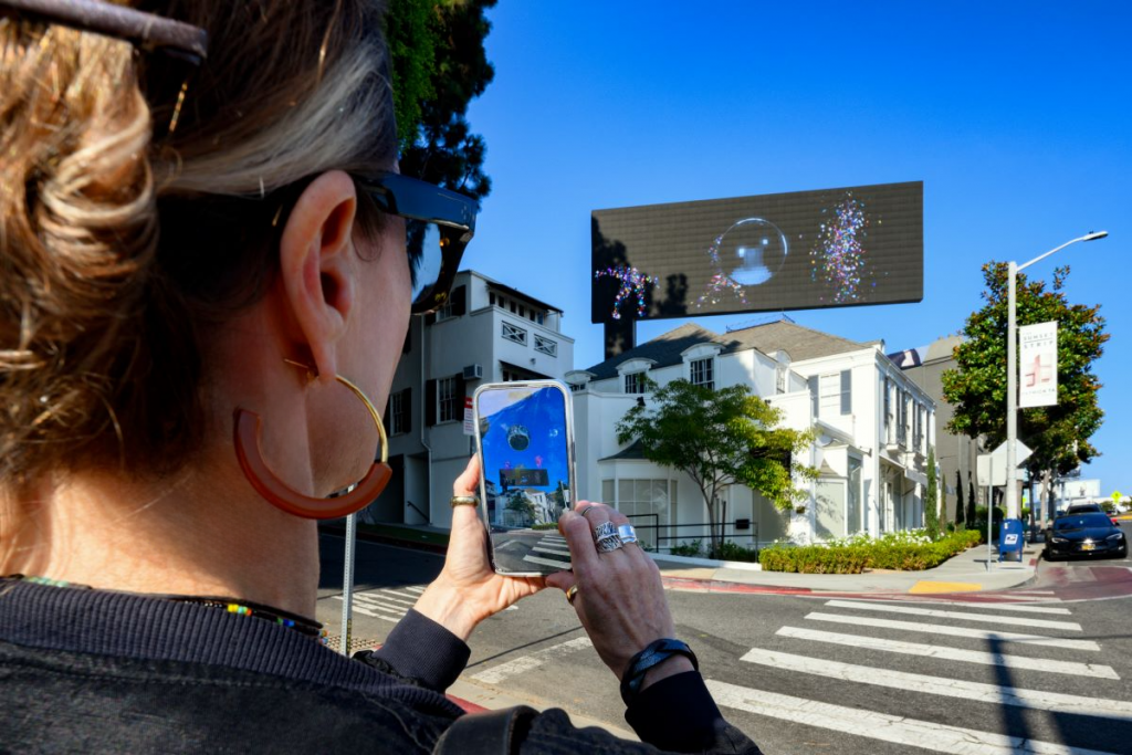 Nancy Baker Cahill, Body Politic (2024) on a billboard on the Sunset Strip in Hollywood, with the artist using her 4th Wall app to view the work's augmented reality component.