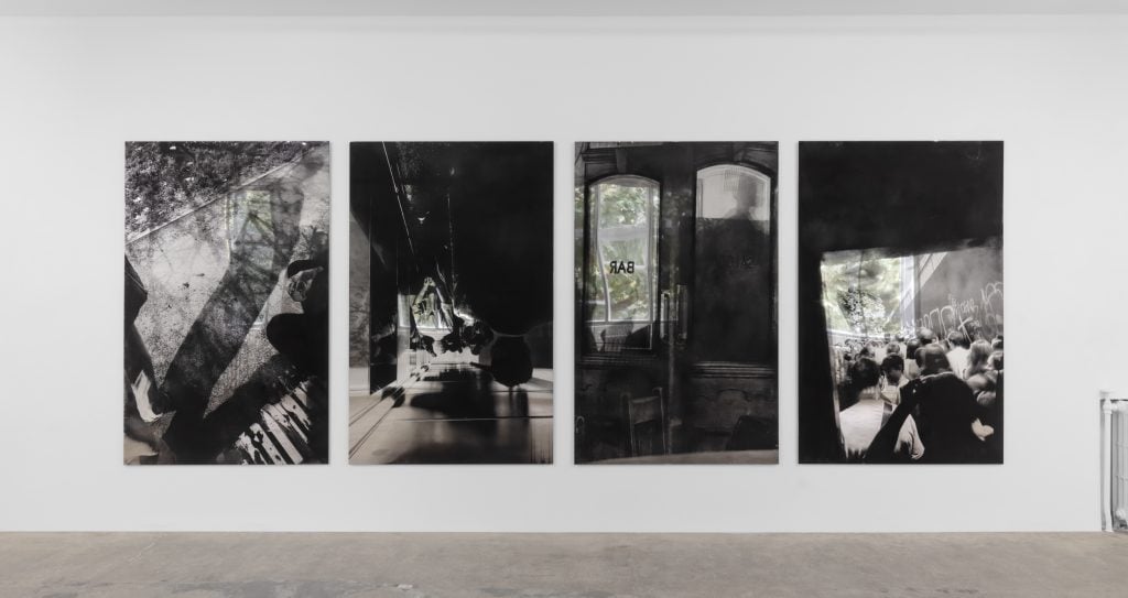 four large portrait oriented black-and-white photographs hanging on a white gallery wall