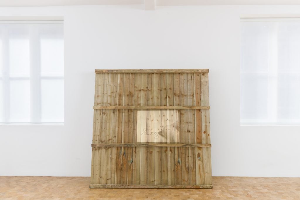 Large wooden panel installation leaning against a white wall in a minimalist gallery space