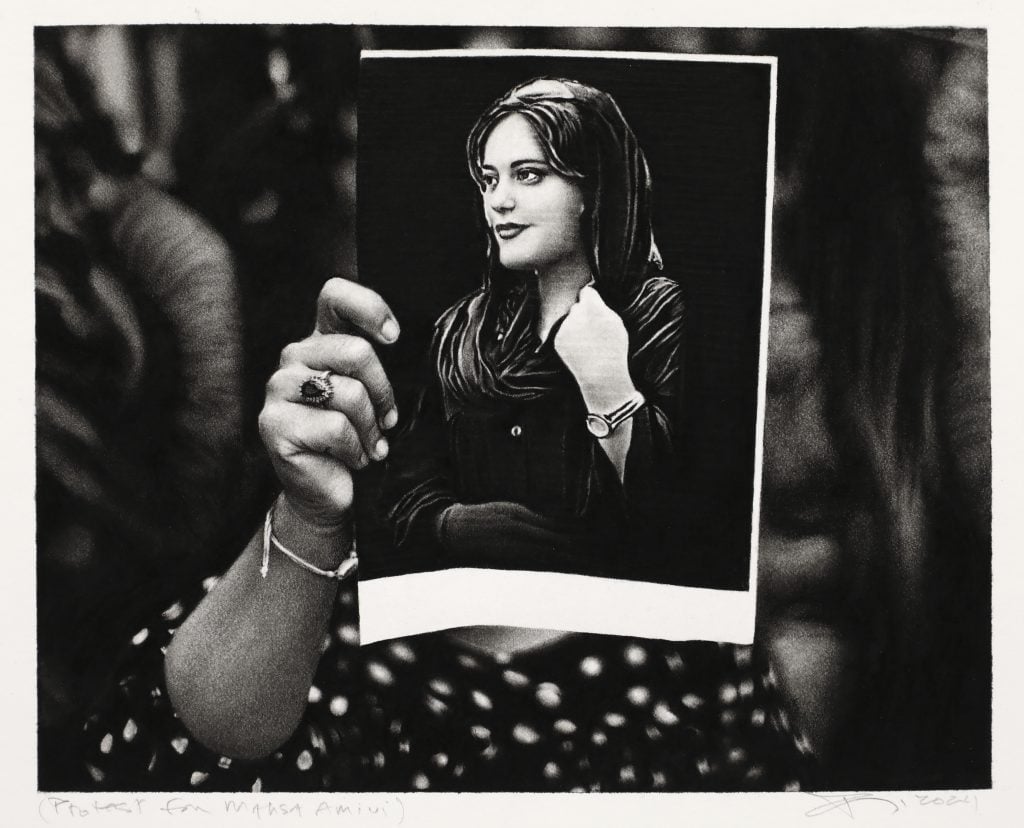 A detailed black-and-white drawing of a person holding a photograph of Mahsa Amini. The person holding the photograph is anonymous, with the focus entirely on Amini’s portrait, which contrasts against the darker background.