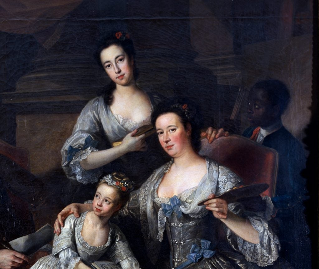 a section of a large traditional family portrait showing three white female members of the family in formal dress and behind the chair a young smartly dressed Black boy