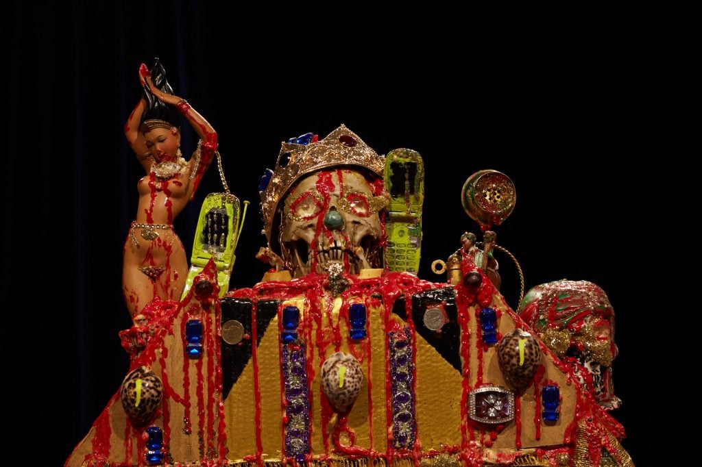 a gold and red sculpture featuring a skull wearing a crown