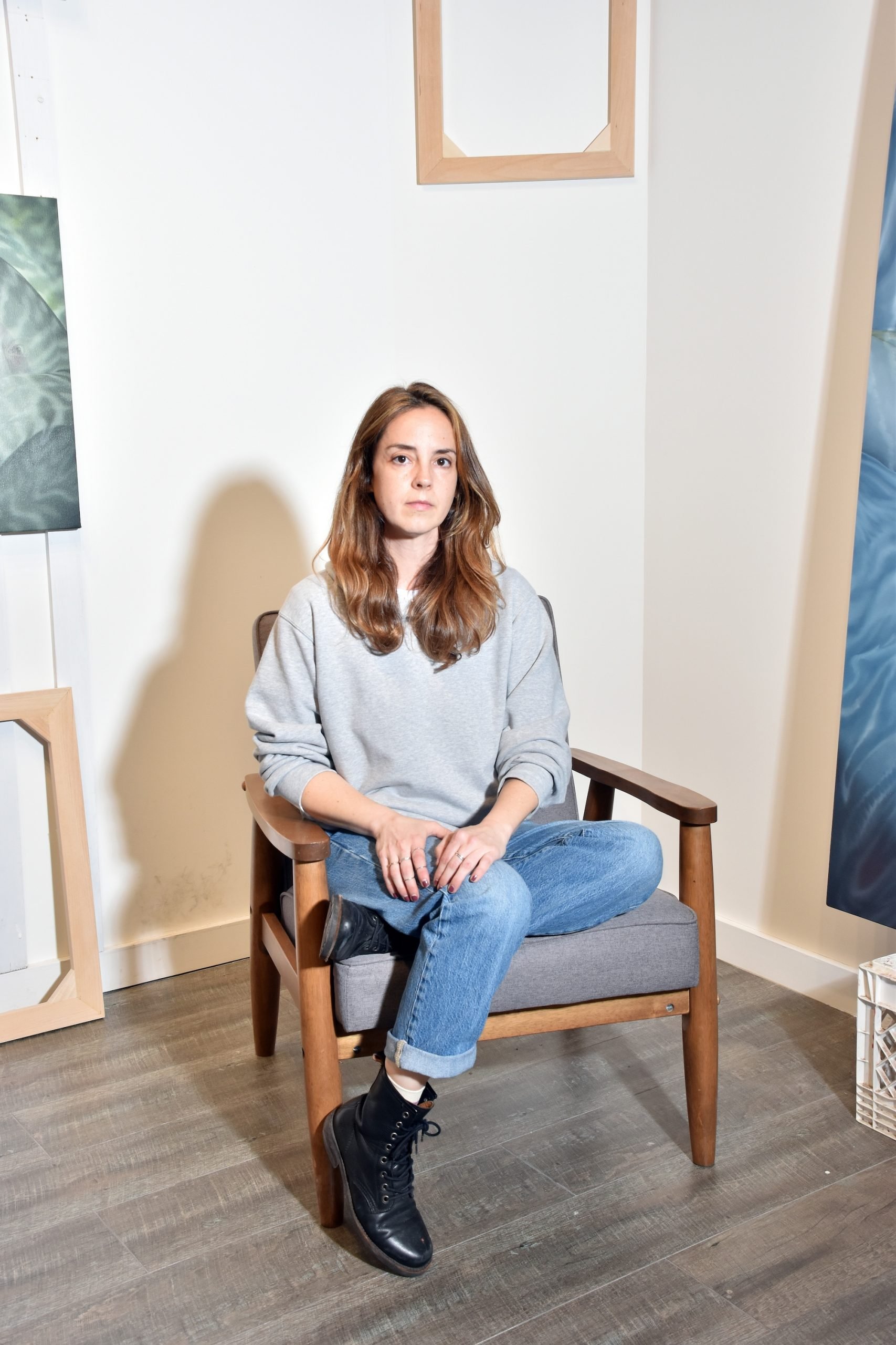 a white woman in her 30s in a chair in an art studio wearing jeans and gray top