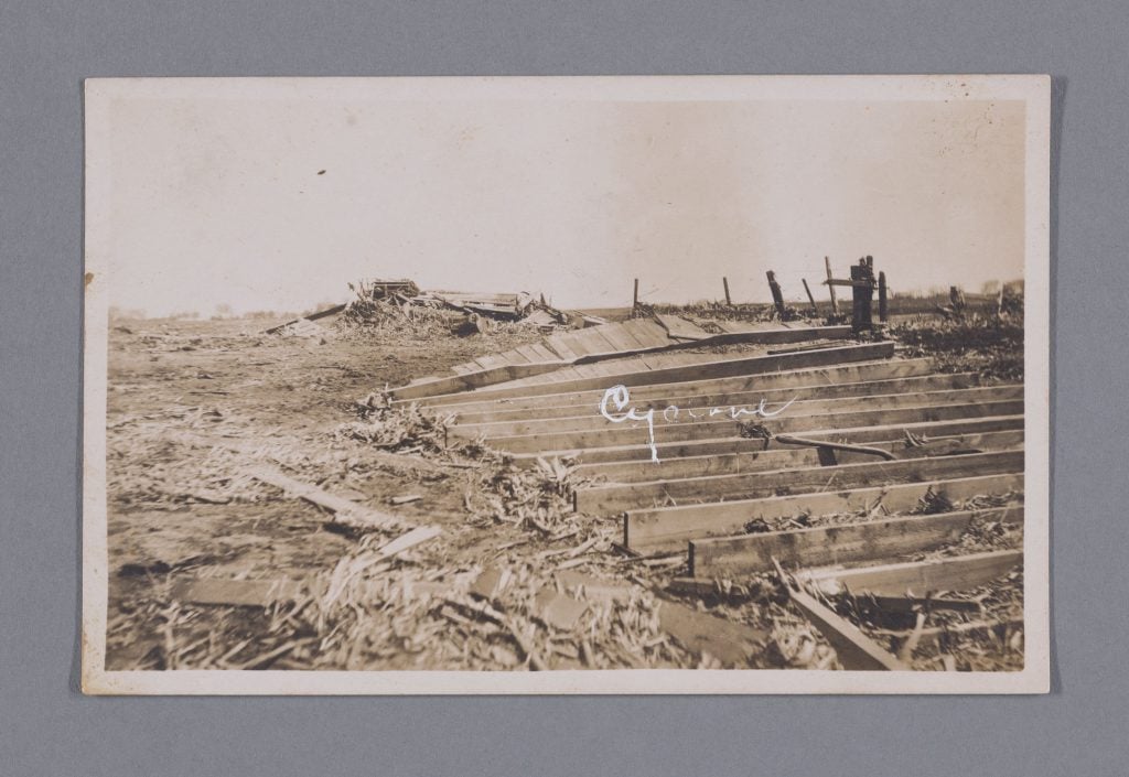 A vintage post card of the aftermath of a natural disaster, with the word cyclone written over the sepia-toned image in white cursive script. 