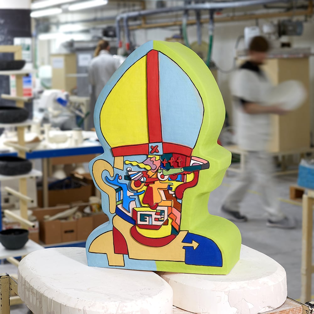 A colorful bust of a Pope by Robbie Williams, the subject's face filled with psychedelic panels, sitting on a stool in a workshop