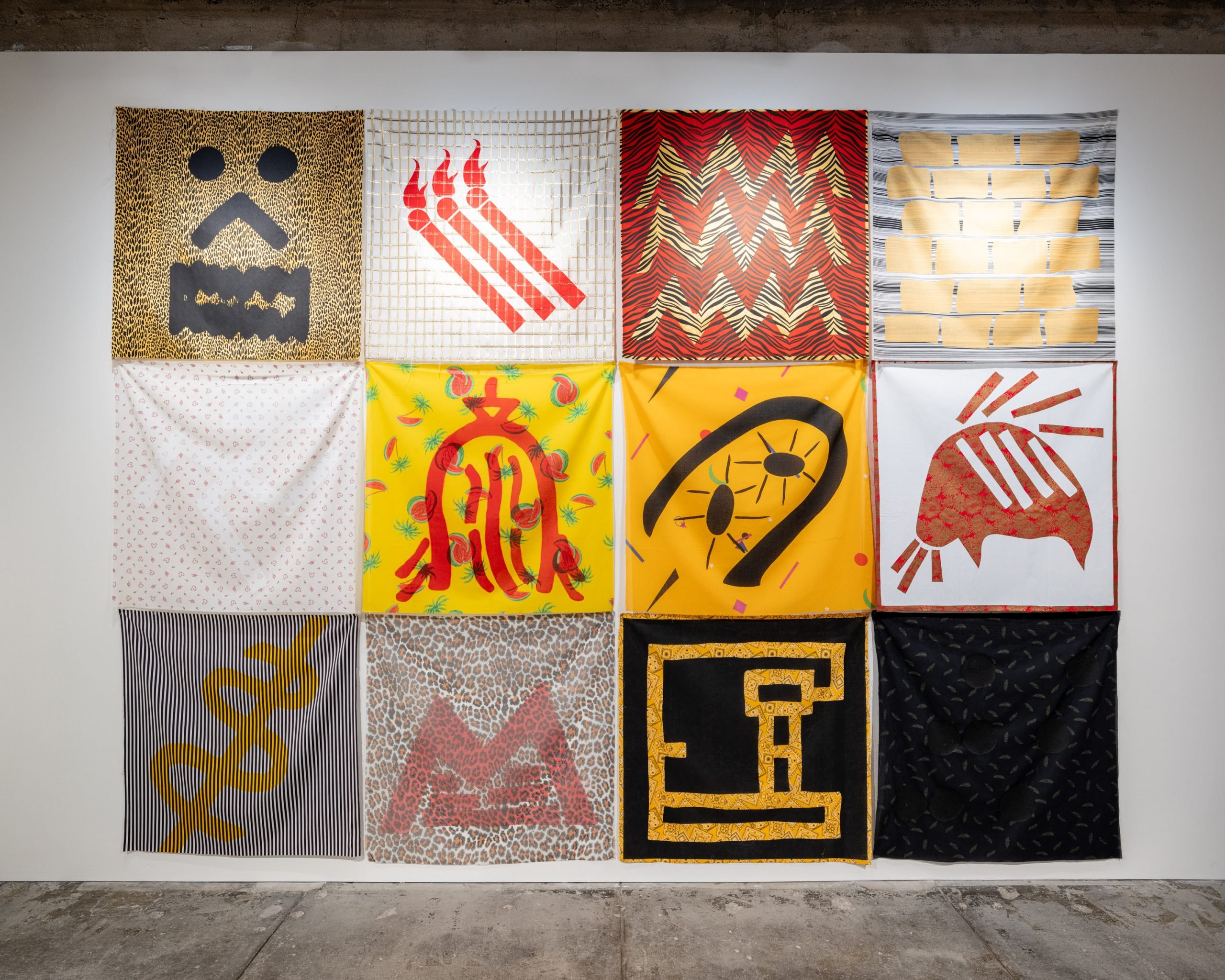 Tina Girouard in collaboration with the Fabric Workshop and Museum, Philadelphia, Conflicting Evidence, (1980) on view in "Tina Girouard: Sign In" at the Center for Art Research and Alliances, New York. A four-by-three grid of fabric panels, silkscreened with symbols devised by the artist.