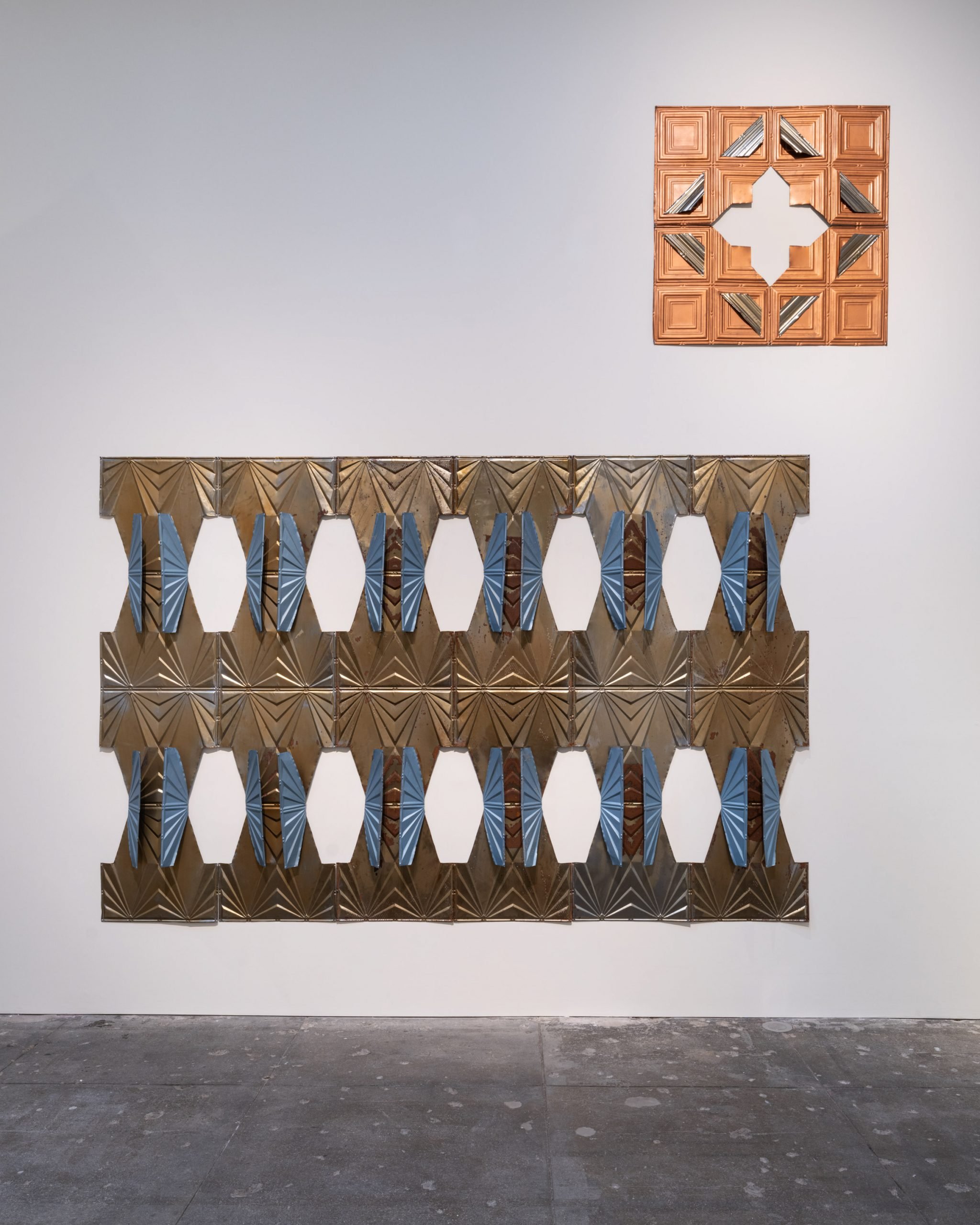 Tin ceiling works on view in "Tina Girouard: Sign In" at the Center for Art Research and Alliances, New York. The two works, made of tin ceiling panels with cut out patterns in them, are mounted on a wall.