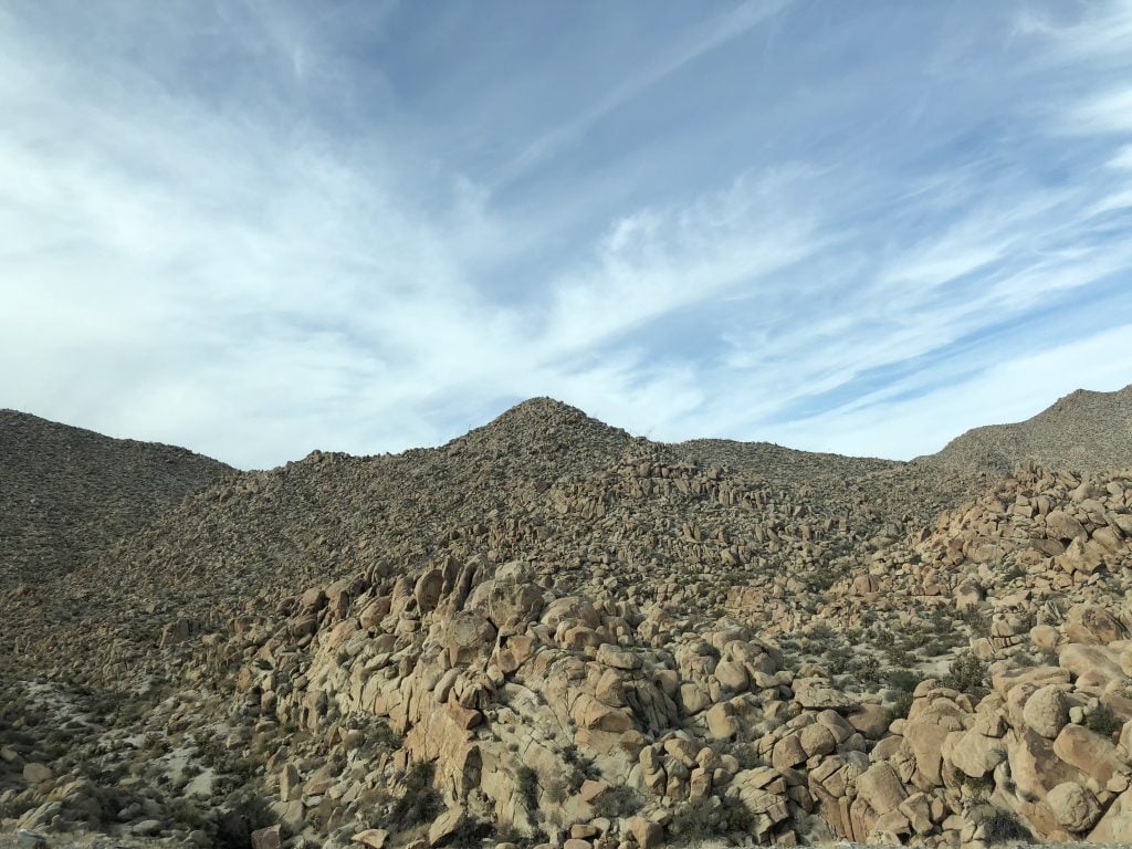 The U.S.-Mexico border, with blue, cloud-streaked skies above a rocky desert landscape.. 