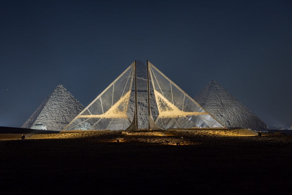 a geometric triangular structure is situated in front of the pyramid, echoing its form.