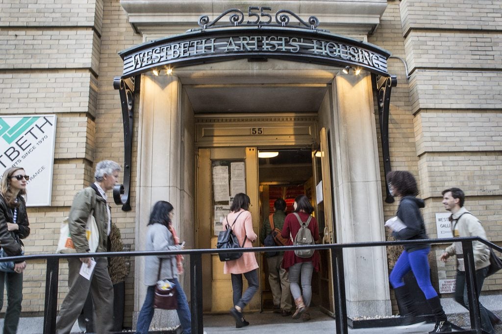 The entrance of Westbeth Artist Housing. People are walking up a ramp to enter a prewar Manhattan apartment building.