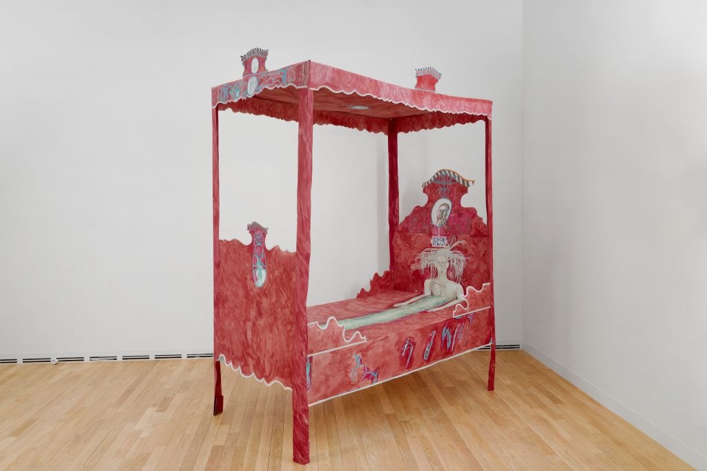 A paper sculpture of a canopy bed covered in red scribbles and the depiction of a to-scale mermaid laying in it, by artist Agnes Scherer and featured at Art Basel Paris in the booth of gallery sans titre.