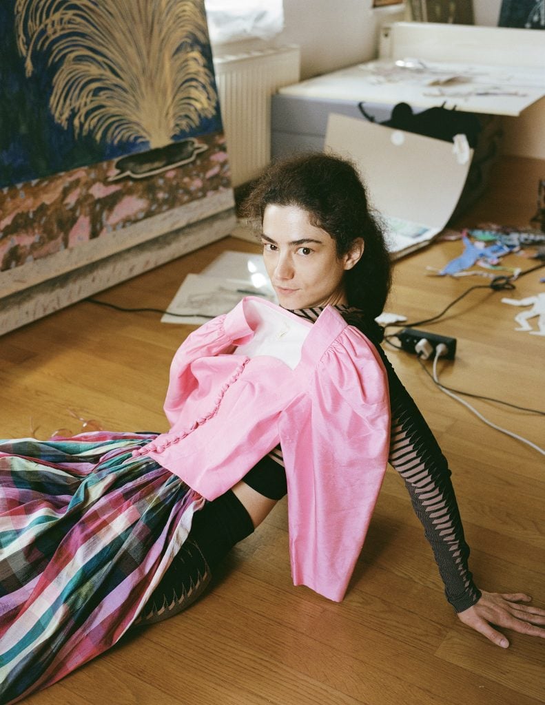 Portrait of artist Agnes Scherer leaning back on the ground with a dress with pink bodice and puffed sleeve and multicolor stripped skirt lain on top of her.